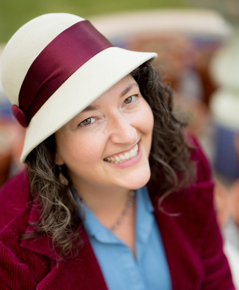 Yvette Keller, laughing in a grey hat and burgundy jacket with matching satin hat band.