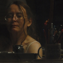 Woman taking picture in a window reflection, a mug of pens, pencils and markers to the side