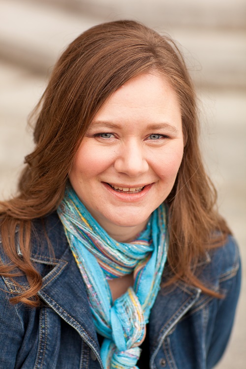 a white woman with long, brown hair wearing a denim jacket and blue scarf
