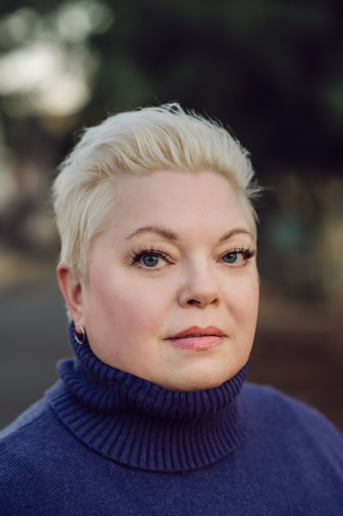 Headshot of a white woman with short blonde hair wearing a purple turtleneck sweater.