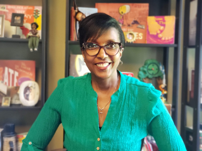 alt= author is a black female with short hair, glasses and smiling face with books in background