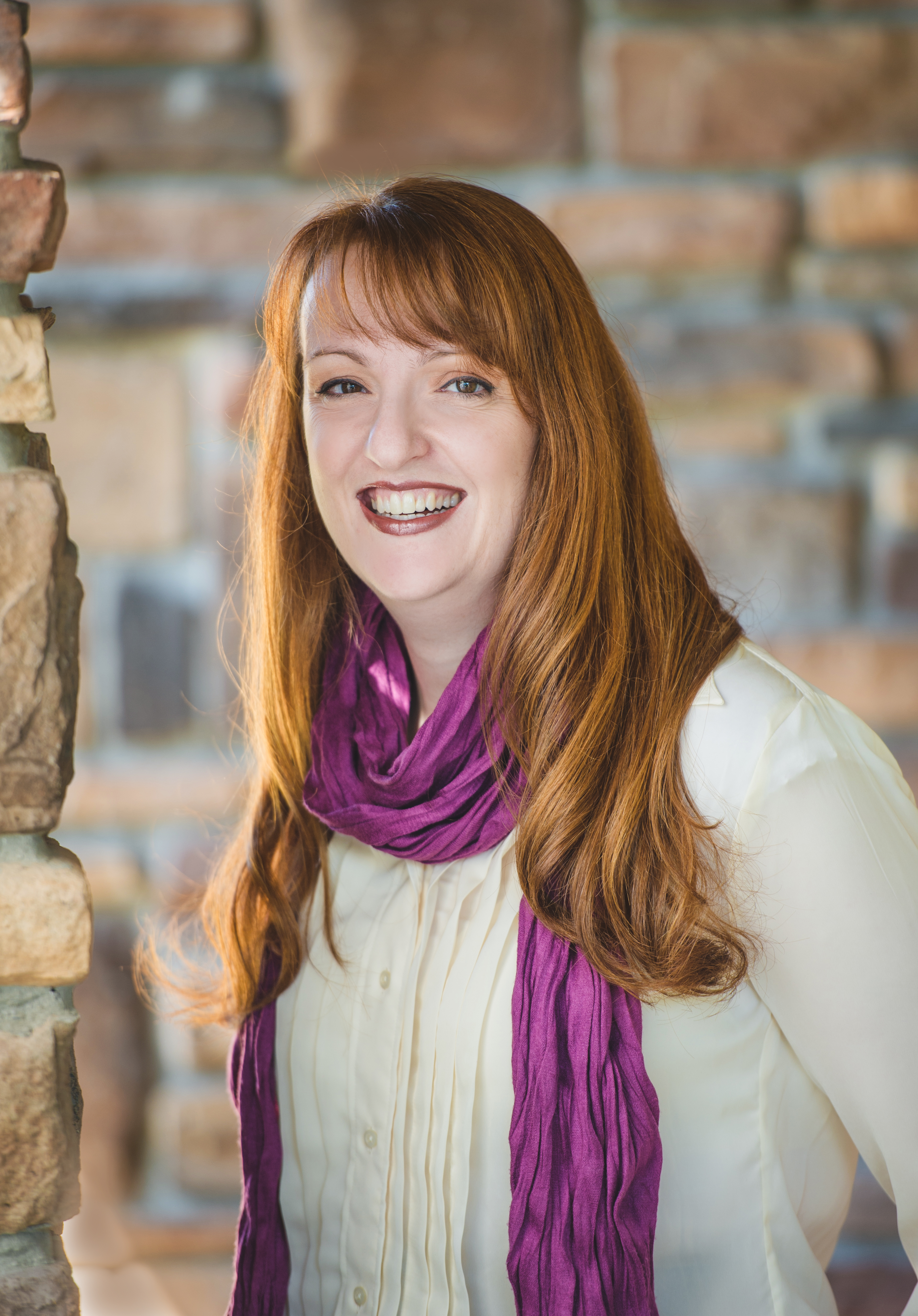 Photo is of a red-haired woman wearing a purple scarf and white blouse. 