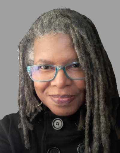 photo of African American woman smiling with gray and brown locs and blue framed glasses