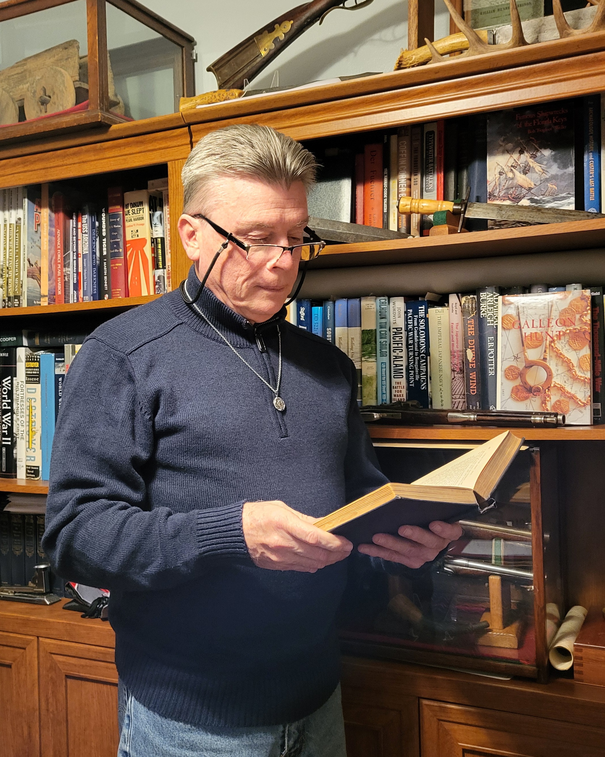 Knight standing with a studied look into the pages of a book in his library with full bookshelves and some historical artifacts in the background