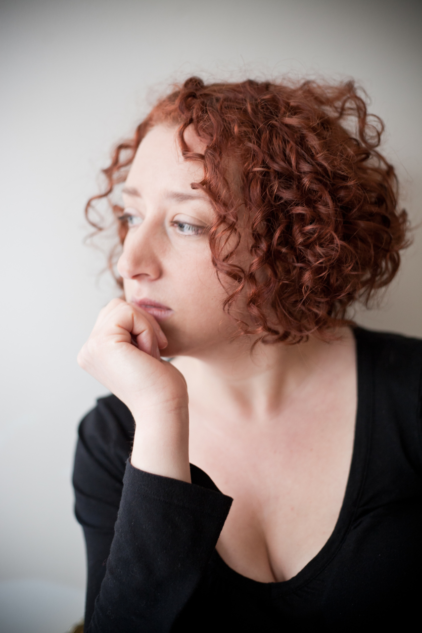 white woman with curly red hair in 3/4 profile, wearing black vneck top