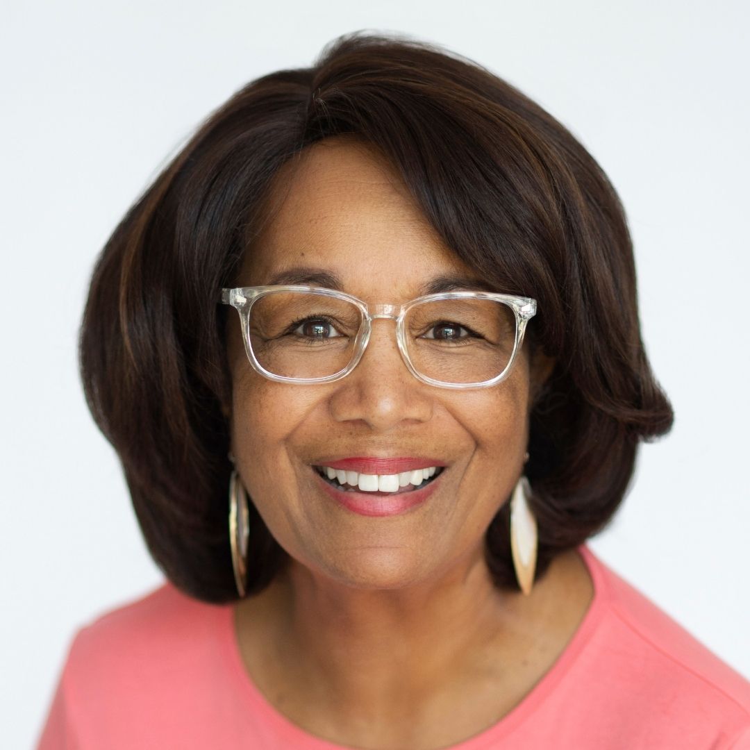 alt tage=Color photo of author Patricia Raybon, showing a big smile, and wearing a coral-colored top, white elongated earrings, eyeglasses with clear-colored frames. Her hair is dark brown in a shoulder-length, pageboy style.