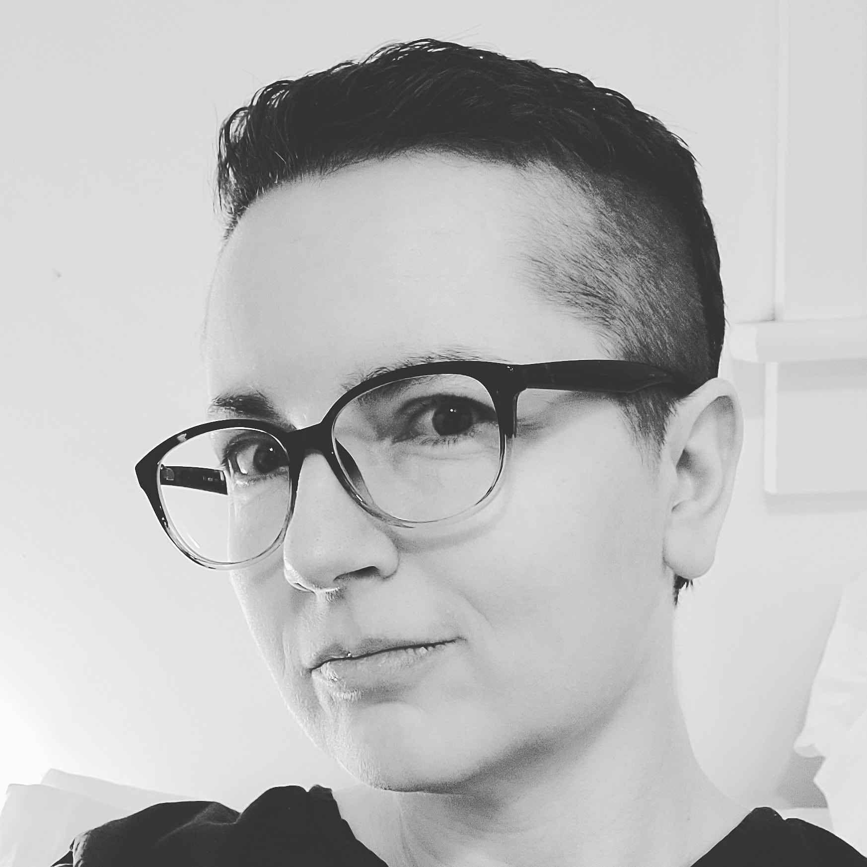 A nonbinary author with short hair and glasses with a slight smile.