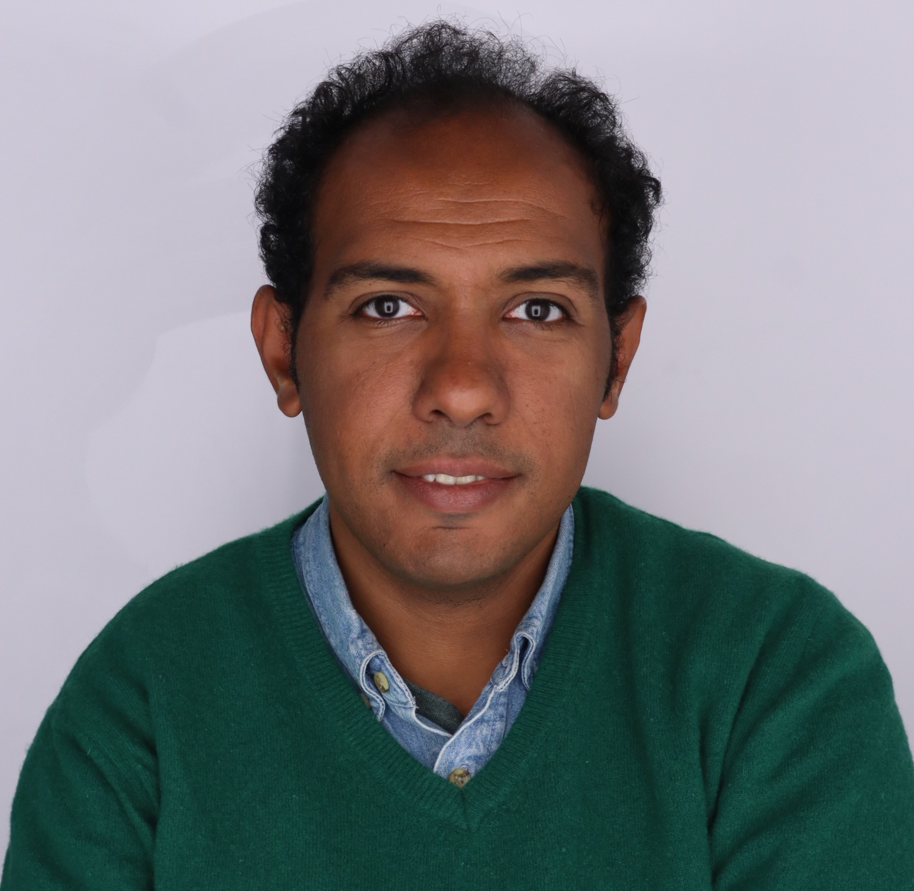 Portrait of Ahmed Hamed wearing a jeans shirt and a green pullover. The person has a rich dark skin tone