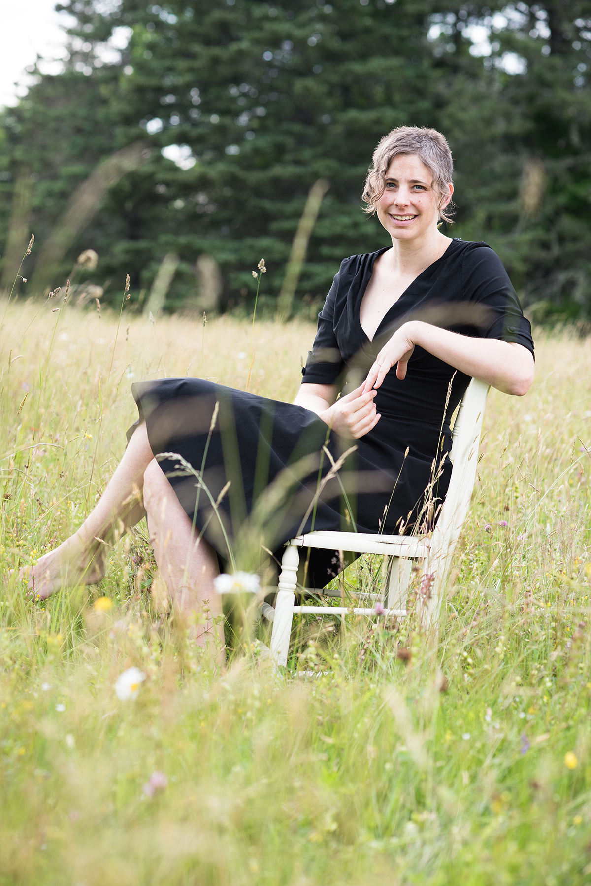 Author sitting on a wooden chair in a field in Maine