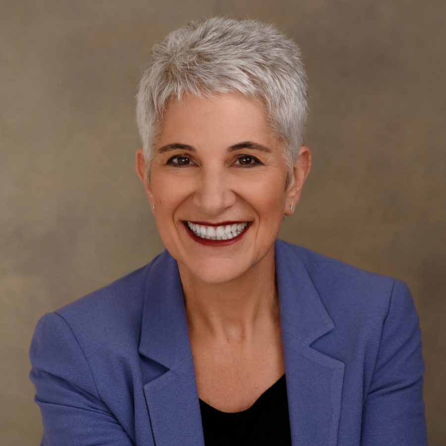 Headshot of Minette Norman, a white woman with short silver hair, wearing a black t with a periwinkle blazer.