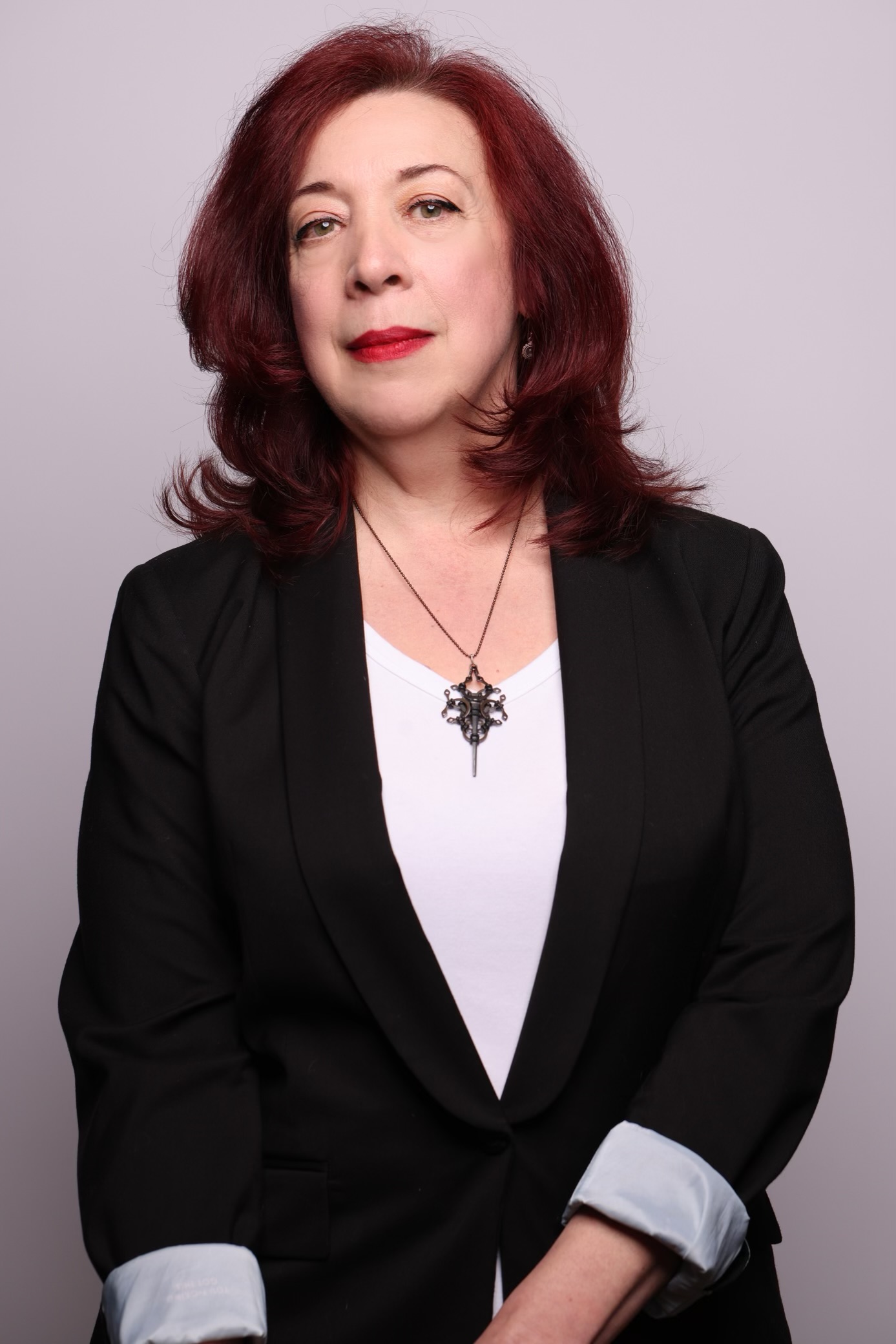 Maria Alexander, author of horror and the mystery fiction for adults and teens, wearing a black blazer and white T-shirt with a steam punk cross necklace