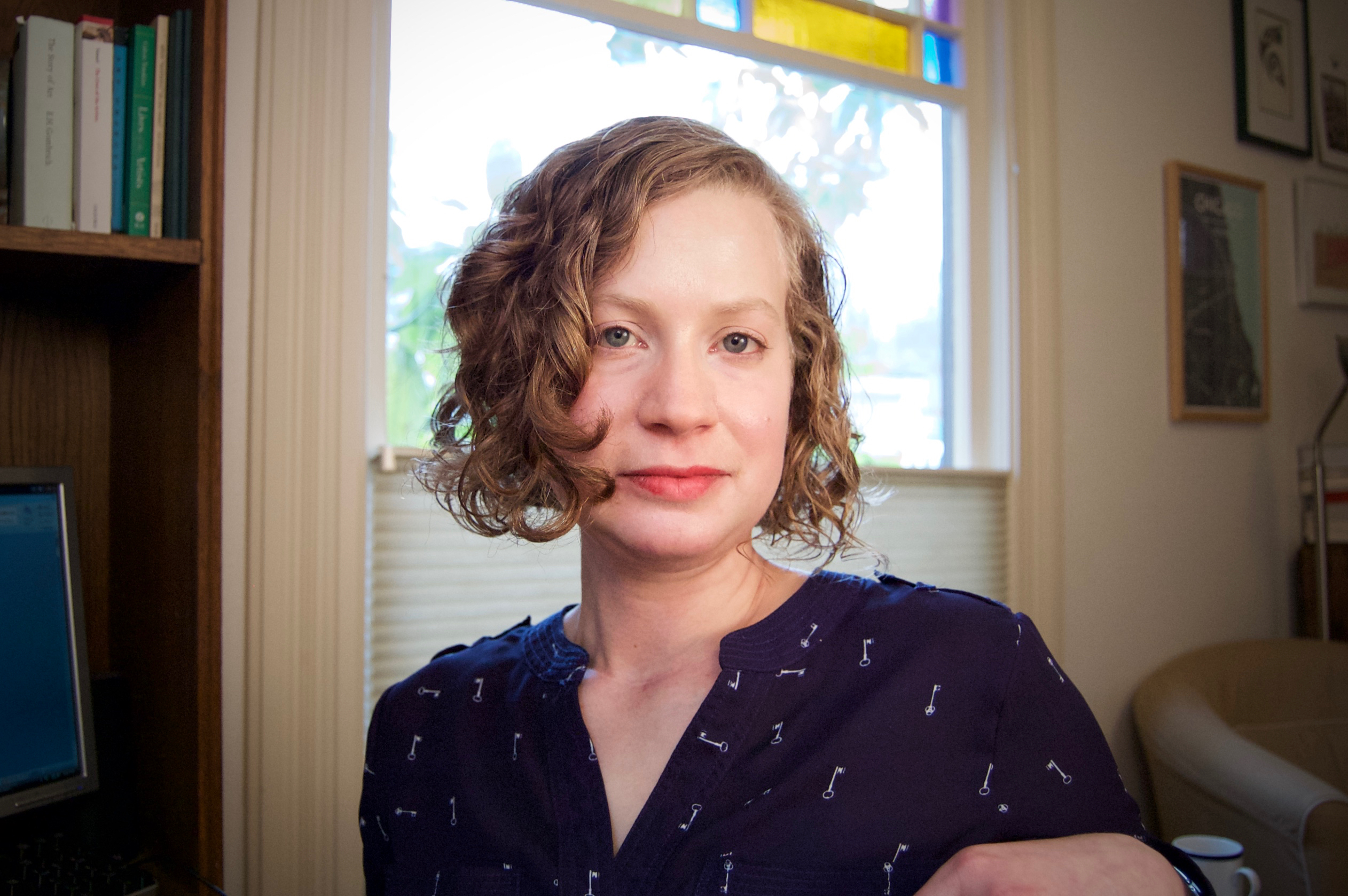 Author photo of Anca Szilagyi, who has a blond curly bob and blue eyes and is wearing a blue shirt.