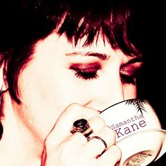 Dark-haired woman drinking coffee from a cup that says Samantha Kane.